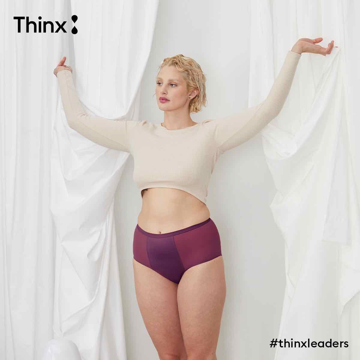 一名模特(金发短发的白人女性)穿着亮紫色“无花果”色的Thinx高腰裤和一件白色毛衣，看着镜头。