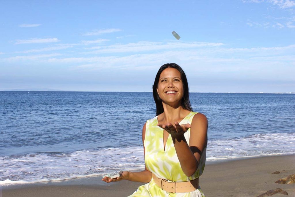 环保型小型护肤品公司Dew Mighty的创始人蒂芙尼·巴扎诺(Tiffany Buzzano)穿着黄色连衣裙走在沙滩上，向空中扔着一根固态精华液。